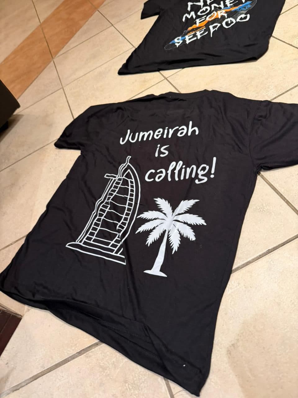 The black Jumeirah Is Calling tee laid flat, back print facing up